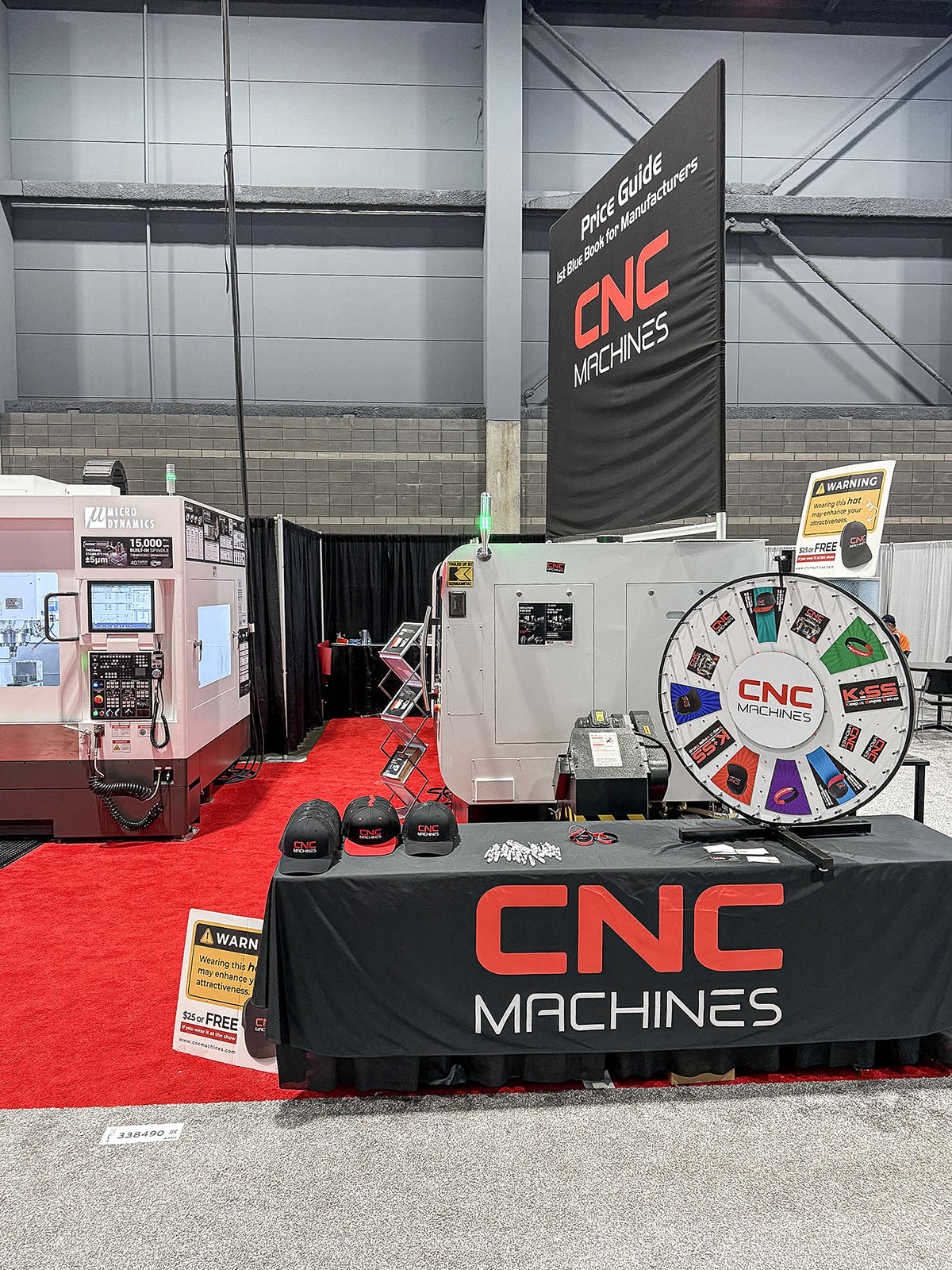 Display do guia de preços da CNC Machines com bonés e material impresso em uma área de expositores da IMTS 2026