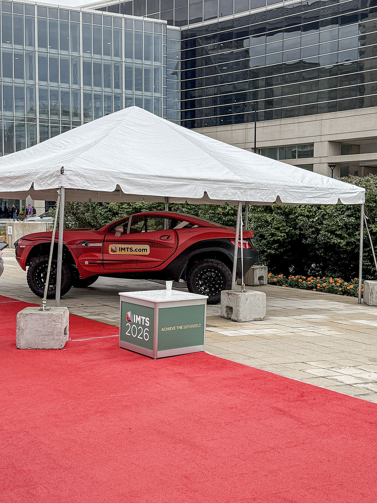 Display de boas-vindas da IMTS 2026 em frente ao McCormick Place, em Chicago, com um veículo vermelho do evento e tapete vermelho