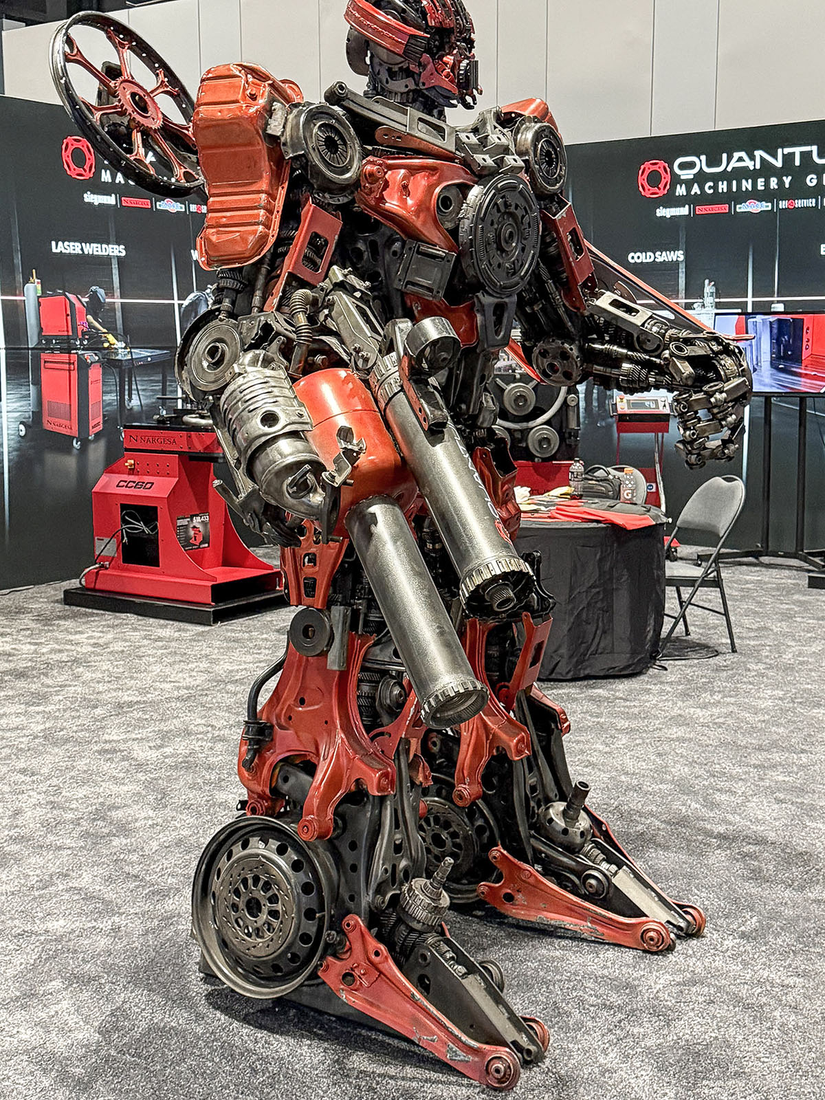 Escultura de robô vermelha e de aço, montada com componentes automotivos, no estande da Quantum Machinery na IMTS 2026